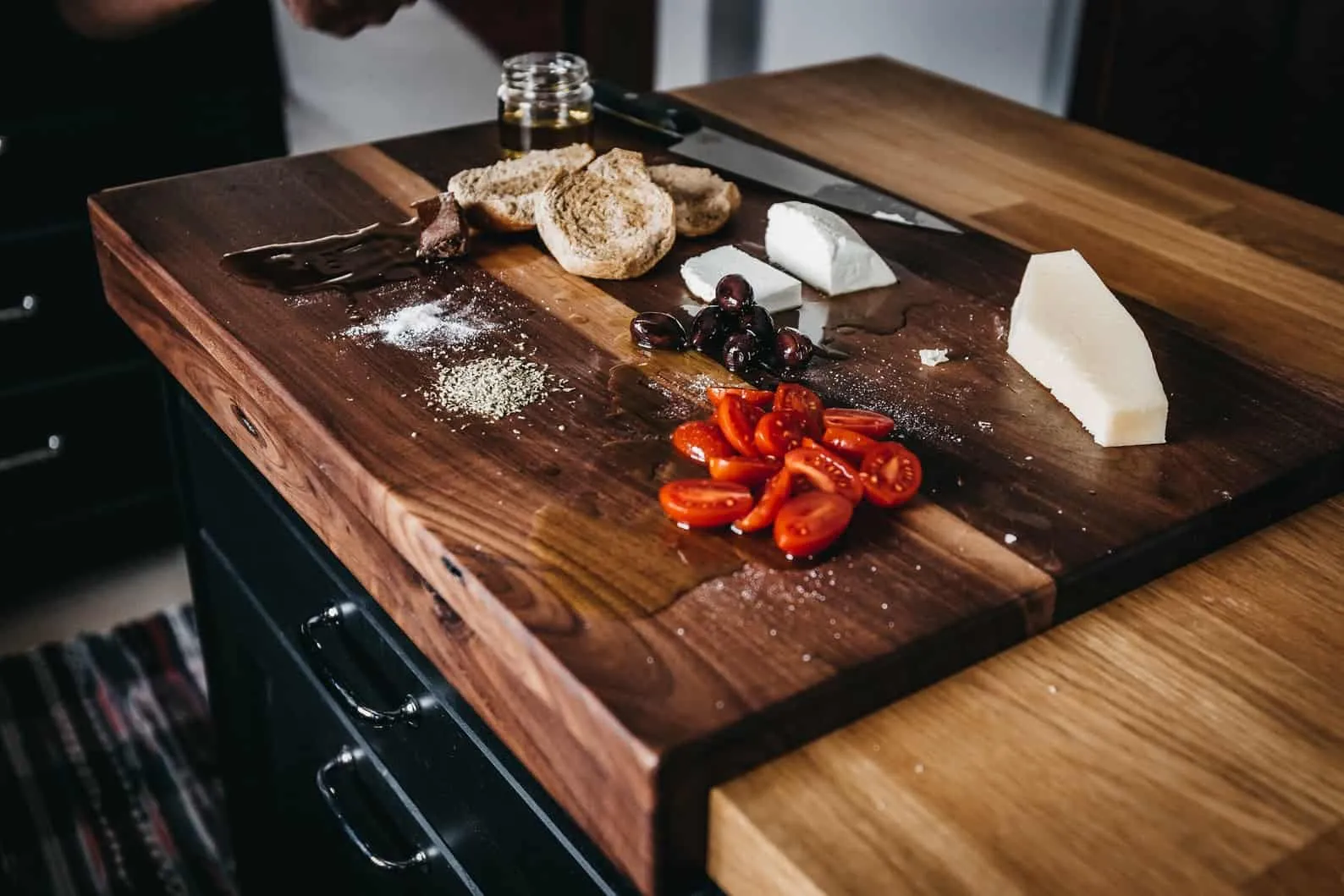 A wooden cutting board with perfectly uniform slices of red bell peppers, green bell peppers, and red onions next to a sharp chef's knife.